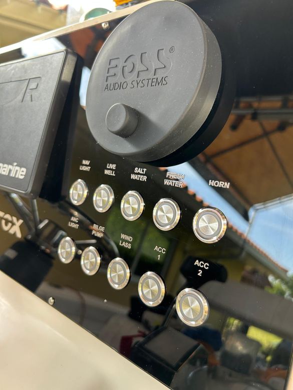 Marine-grade Boss Audio head unit mounted beside a lit stainless switch panel at the helm