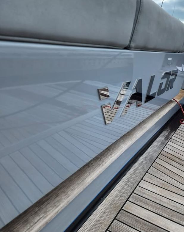 Grey yacht hull polished to a mirror finish reflecting the teak deck